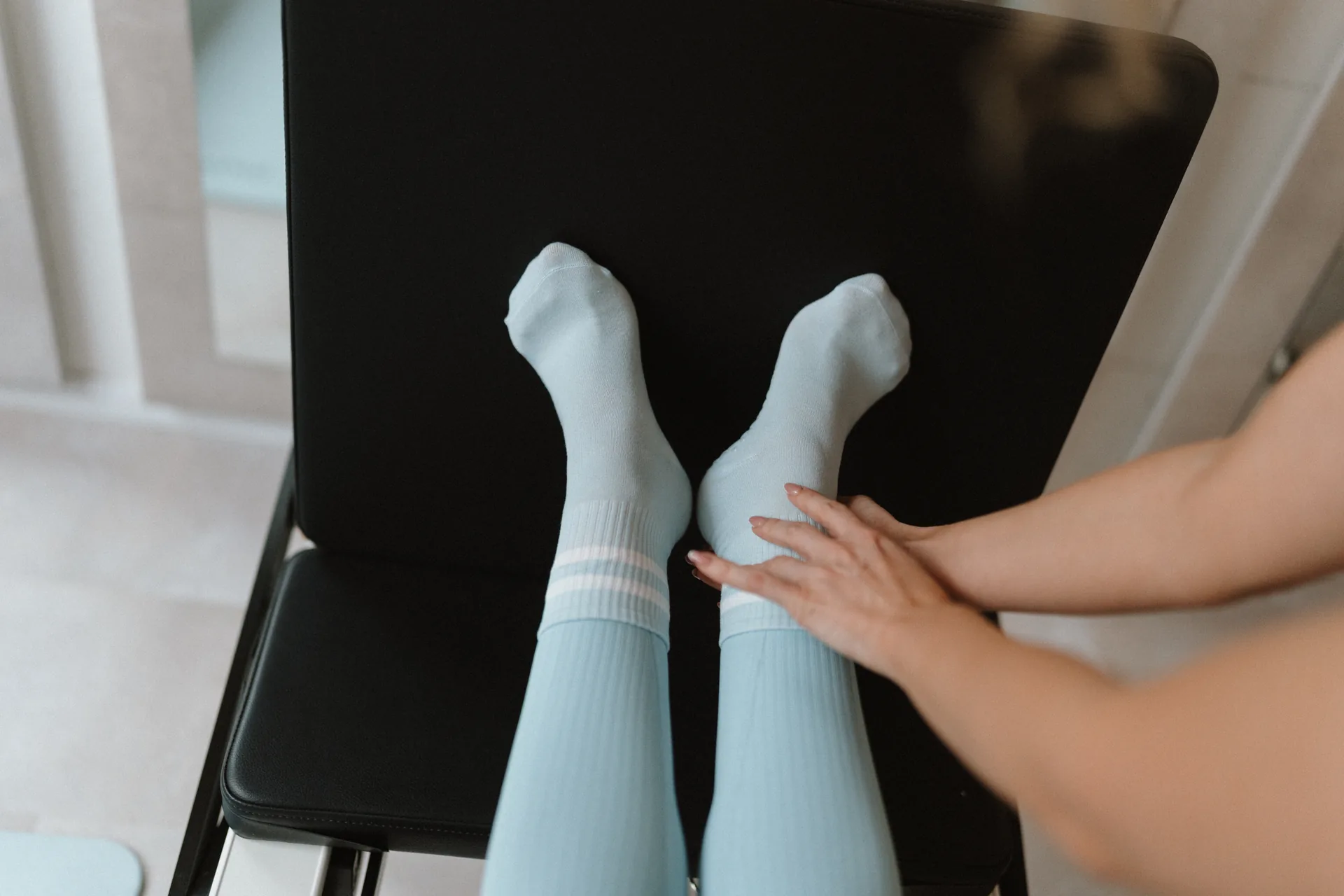 Lábboltozat-aktiválás ellenőrzése reformer pilates közben, oktató keze a vendég bokáján, világoskék zoknis lábak a Pilates’nfinity budaparti stúdiójában.