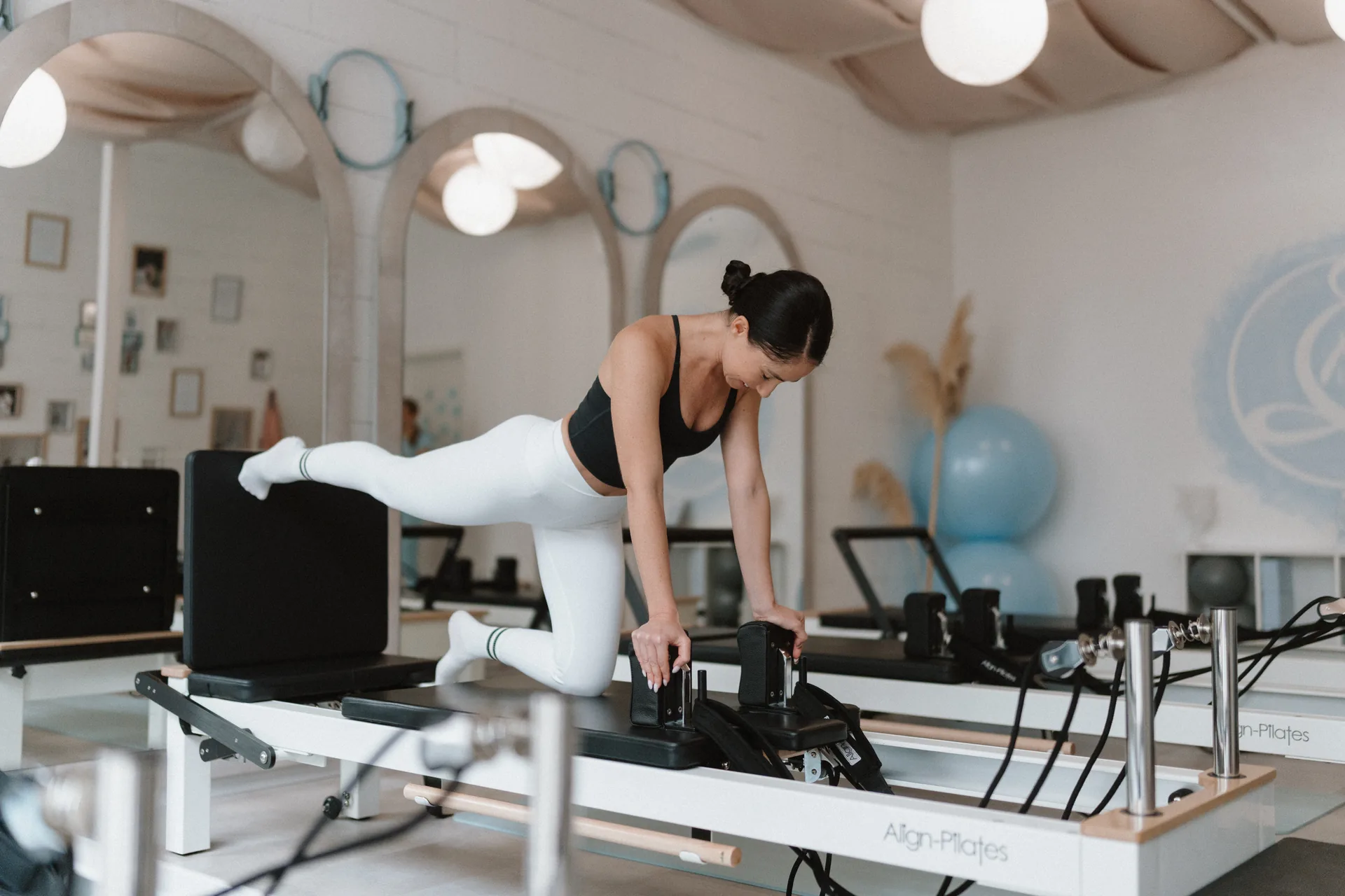 Reformer pilates gyakorlat négykézláb támaszban, nyújtott lábemeléssel és stabil medencével, letisztult stúdiókörnyezetben.