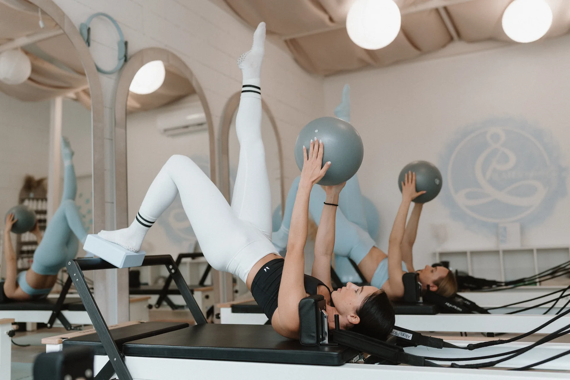 Reformer pilates óra térdvalgus kontroll fókuszszal – vendégek egy lábas híd gyakorlatot végeznek labdával a Pilates’nfinity reformer gépeken.