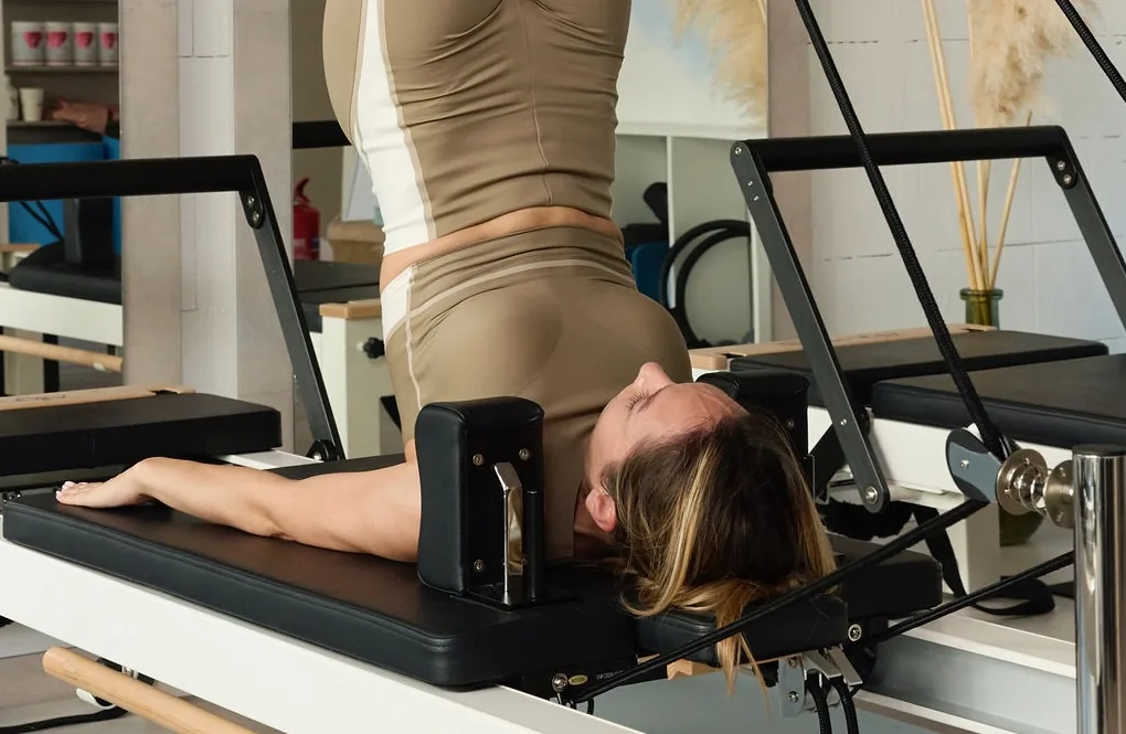 Vendég reformer gépen, csípőemeléses pilates gyakorlatban, kontrollált, derékkímélő mozdulat közben.
