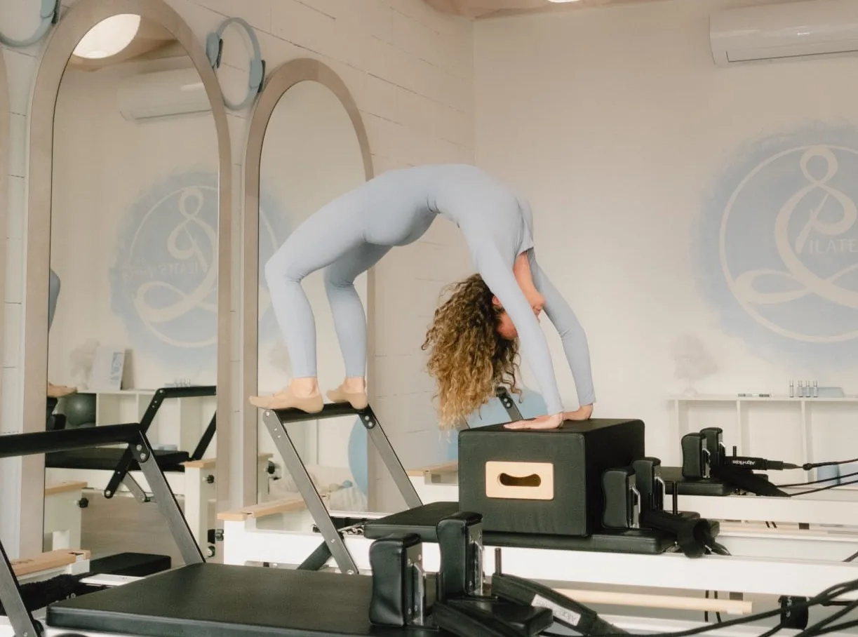 Pilates híd pozíció boxszal a reformeren: íves mellkasnyitás, erős kar- és vállövi támasz, kontrollált gerinchelyzet.