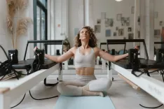 Pilates’nfinity Budapart reformer pilates stúdió: nő ülő mellkasnyitó nyújtást végez a matracon a reformerek között